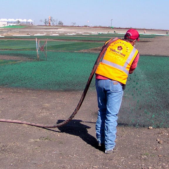 Construction professional hydraulically spreading soil conditioner on bare ground