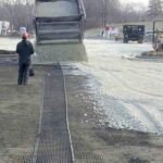 Construction professionals installing aggregate over biaxial geogrid for increased ground support and base stabilization