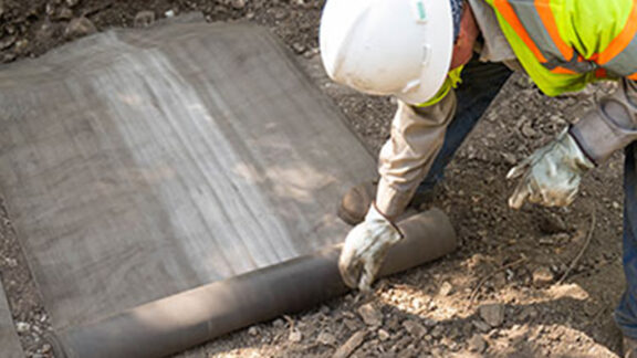 Installing pre-cut strips of concrete canvas as a ditch liner in San Antonia, Texas.